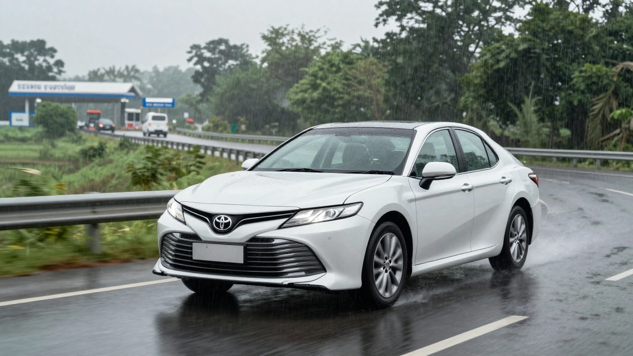 A Camry Hybrid driving on a rainy rural Indian highway with a service center in the distance.